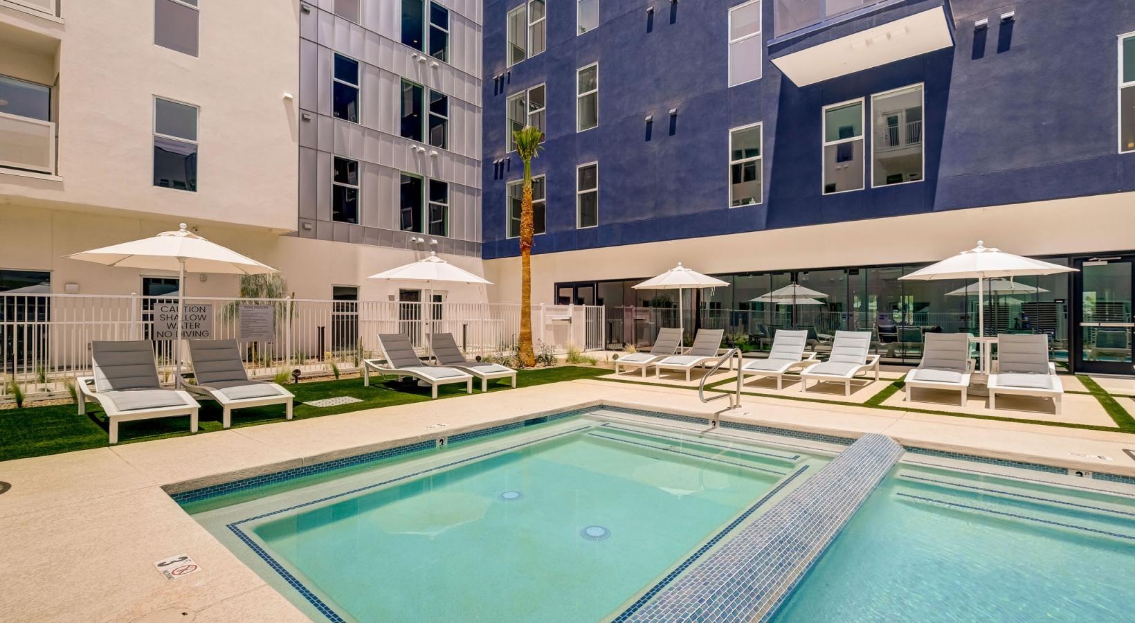 Access to resident-only features a pool with chairs and umbrellas by a building